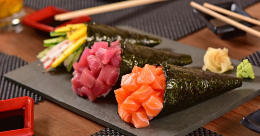 tre temaki sushi su un piatto all'interno di un ristorante giapponese, facilmente distinguibili per la loro forma a cono