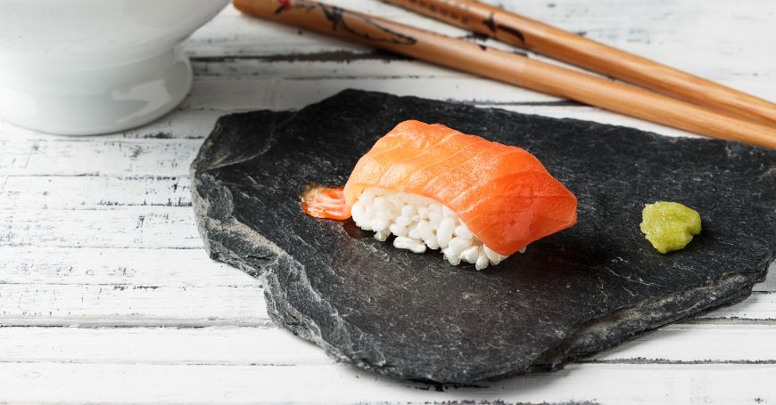 un pezzo di nigiri sake con salmone su un piatto nero e bacchette per il sushi