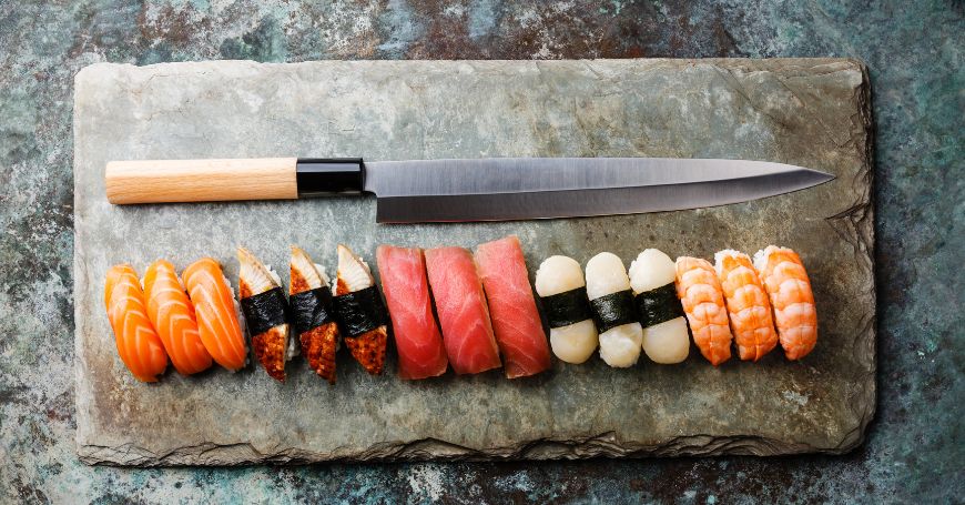 diverse tipologie e varianti di nigiri sushi disposti su un tagliere e un coltello