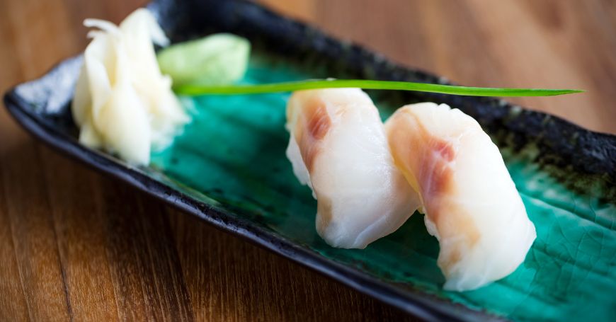 due pezzi di nigiri di branzino, o suzuki nigiri, su un piatto all'interno di un ristorante di sushi giapponese